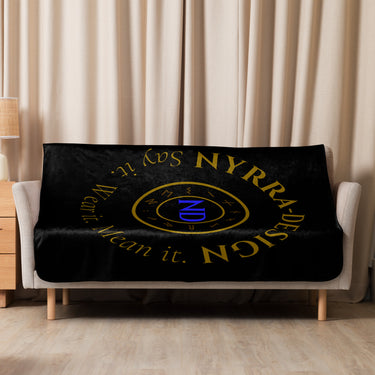 Schwarze Sherpa-Decke mit goldenem NYRRA-DESIGN Logo, dekorativ auf Sofa drapiert