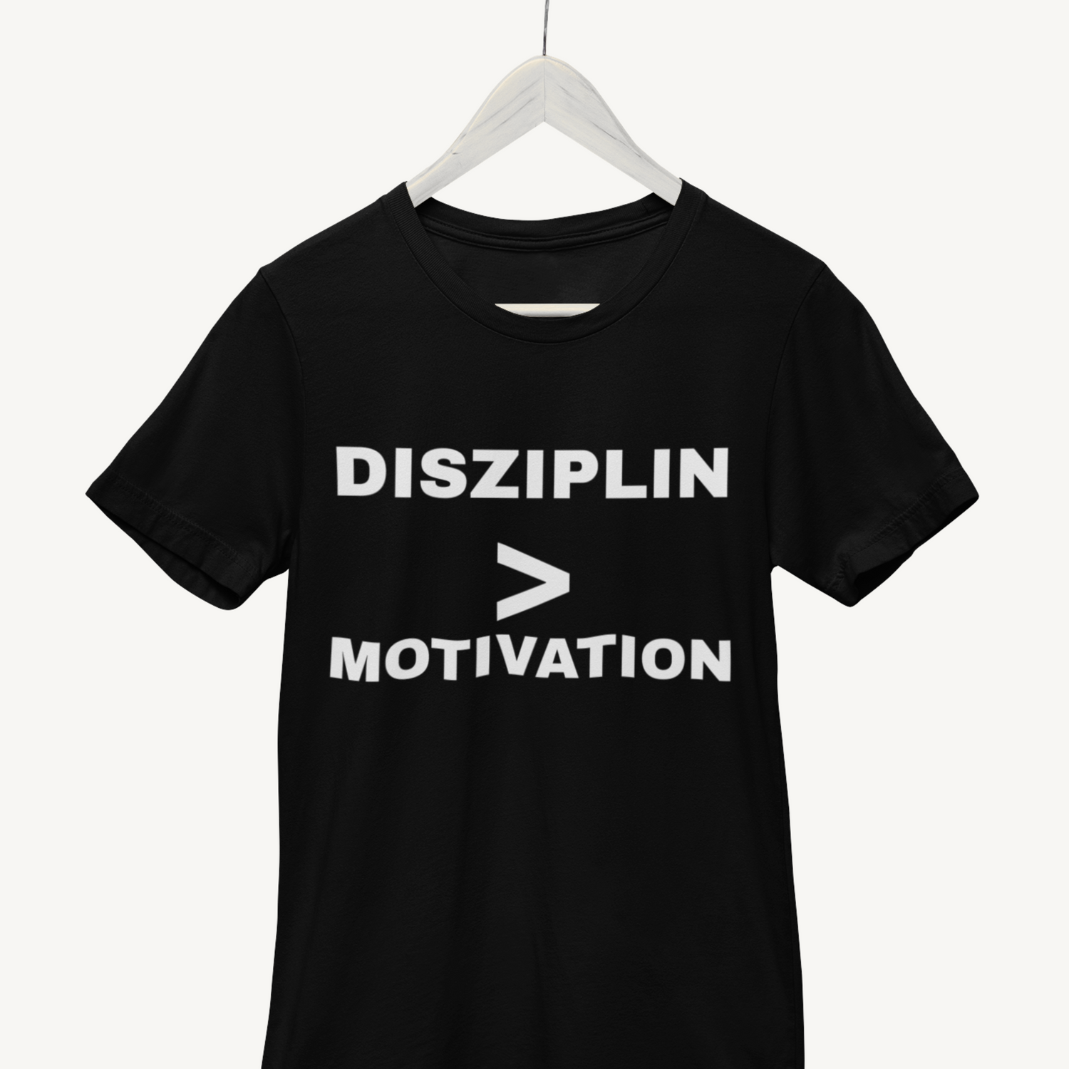 Schwarzes T-Shirt auf Kleiderbügel mit weißer Aufschrift „DISZIPLIN > MOTIVATION“.