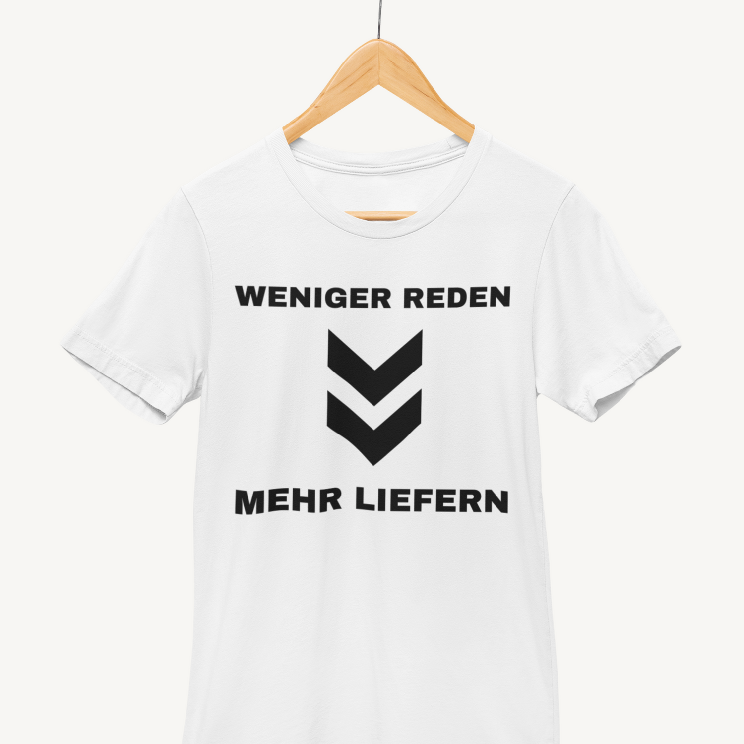 Weißes T-Shirt auf Kleiderbügel mit schwarzer Aufschrift „WENIGER REDEN. MEHR LIEFERN.“ und zwei Pfeilspitzen.