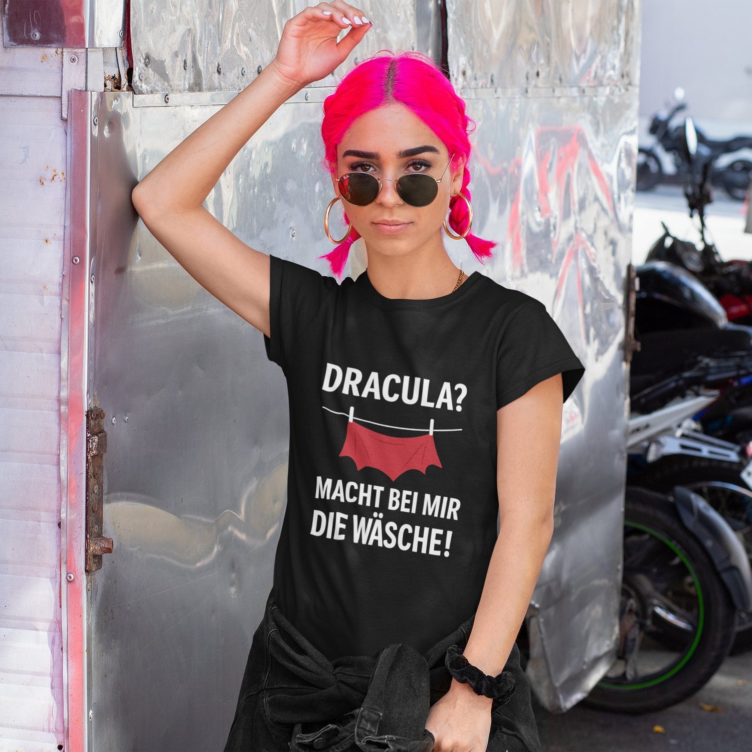 Frau mit pinken Haaren trägt schwarzes Halloween-T-Shirt von Nyrra-Design mit dem Aufdruck „Dracula? Macht bei mir die Wäsche!“.