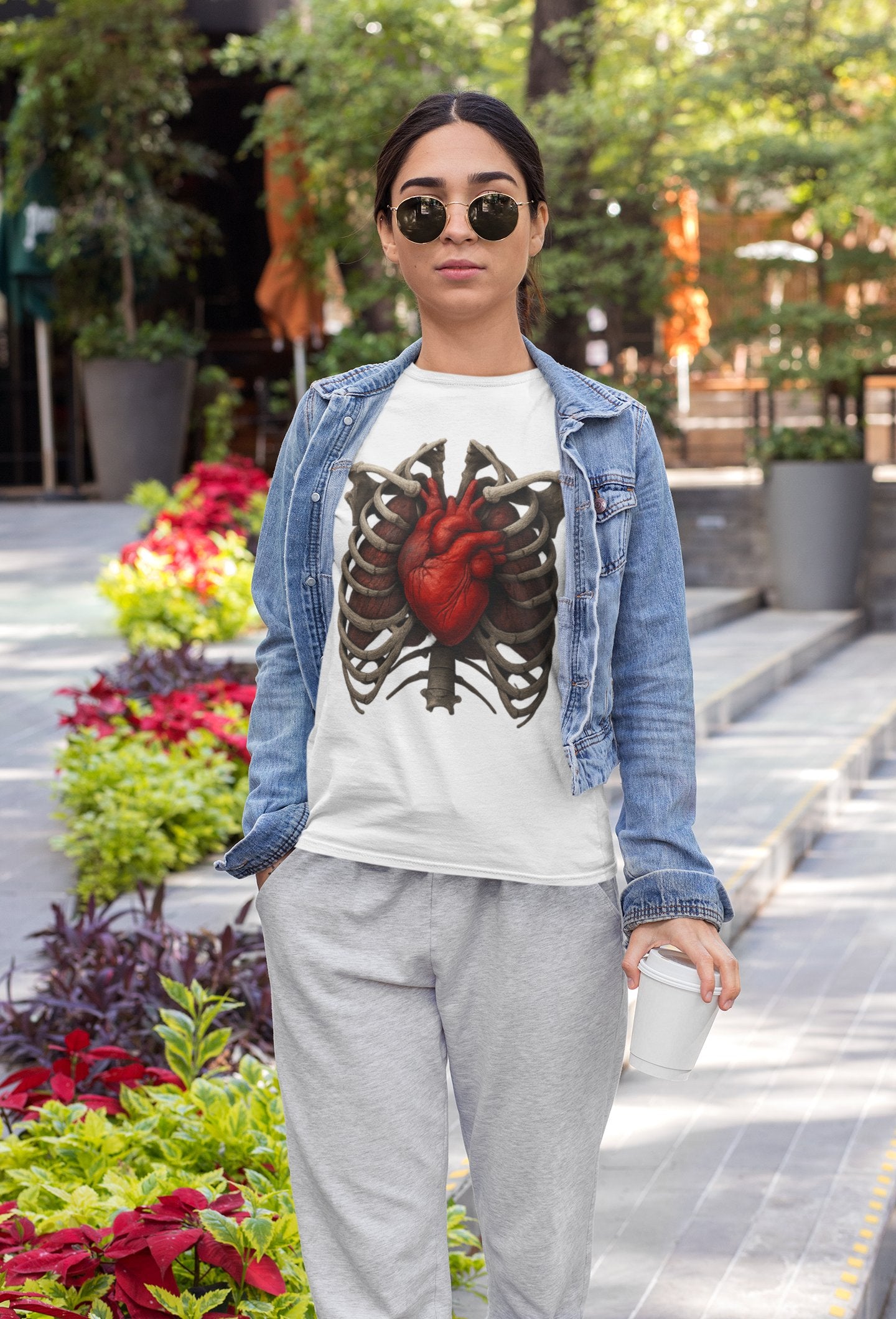 Frau mit Sonnenbrille trägt weißes Halloween-T-Shirt von Nyrra-Design mit anatomischem Herz- und Rippenmotiv.