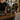 Kundin scannt einen QR-Code-Aufsteller auf einer Café-Theke, während Merch-Produkte und Nyrra-Branding im Hintergrund sichtbar sind. Die Szene zeigt, wie Gäste direkt vor Ort unkompliziert zum Merch-Shop gelangen.